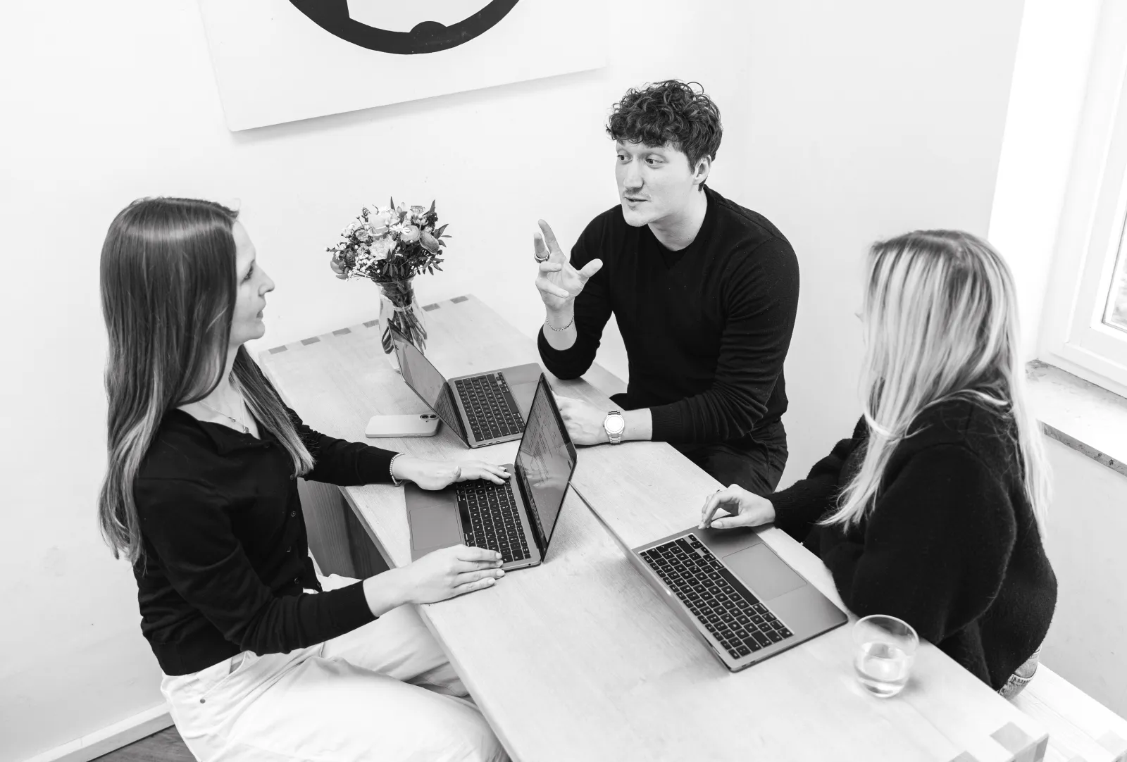 Drei Mitarbeitende von GRAPEVINE arbeiten mit Laptops an einem Tisch und besprechen sich.