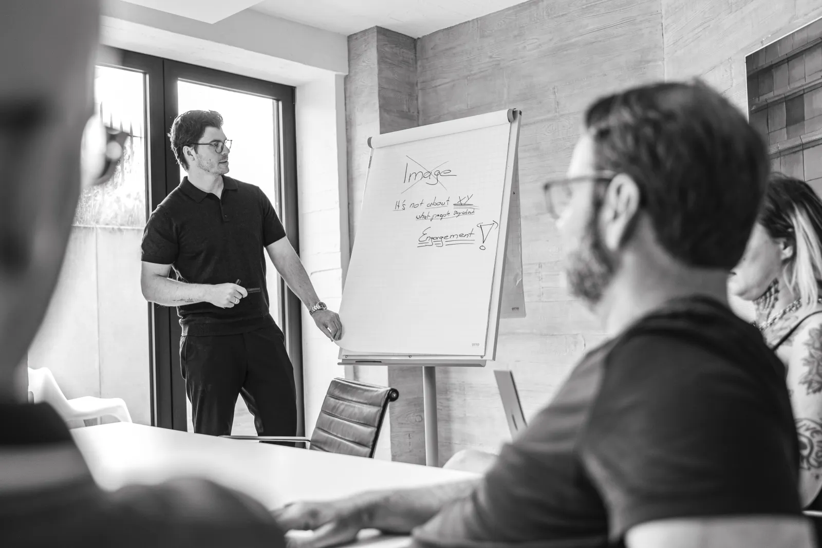 Ein Mitarbeiter von GRAPEVINE präsentiert an einem Flipchart, im Vordergrund hören Kolleginnen und Kollegen zu